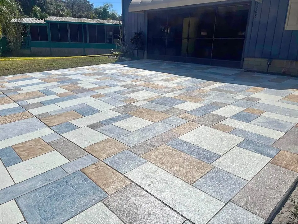 A concrete wheelchair ramp with metal handrails on the right side, leading to a sidewalk. The ramp, constructed by Apex Concrete Albuquerque, is slightly inclined and bordered by a low concrete wall. Surrounding the ramp are patches of green grass and some pavement stones.